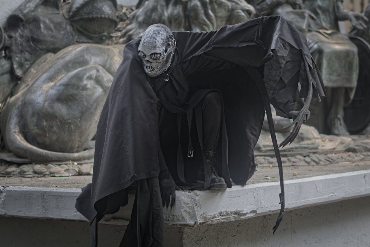 A mysterious figure in dark, theatrical costume crouches by a dramatic sculpture, enhancing a sense of mystery.