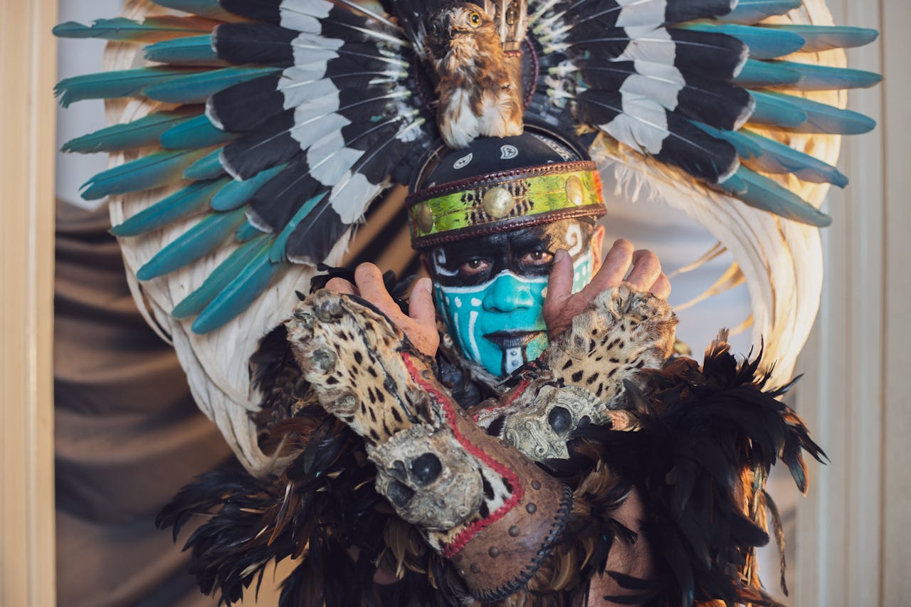 Man in ornate tribal outfit with feathered headdress and painted face, striking pose.